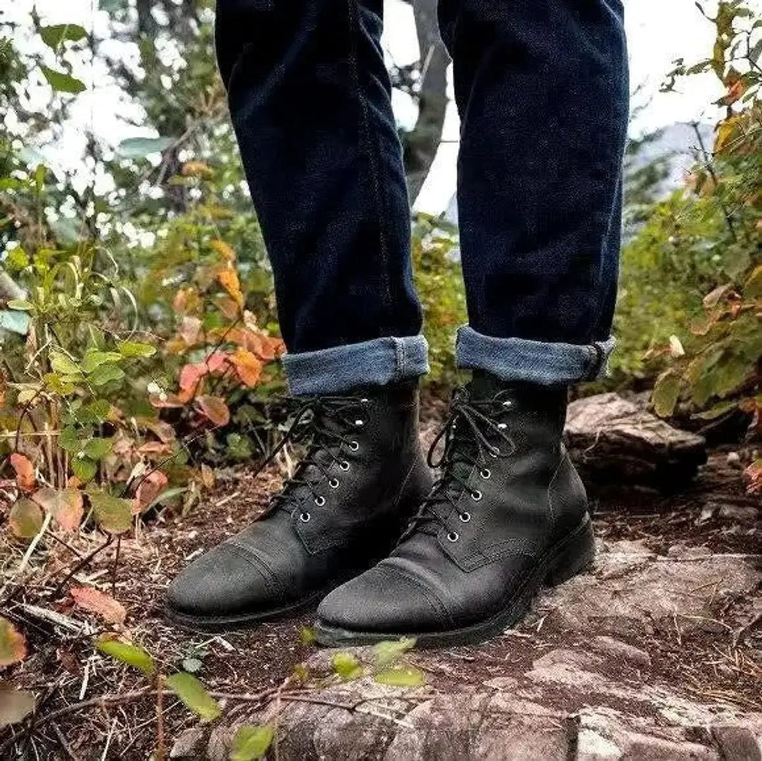 Black cap toe boots worn with turned-up trousers outdoors