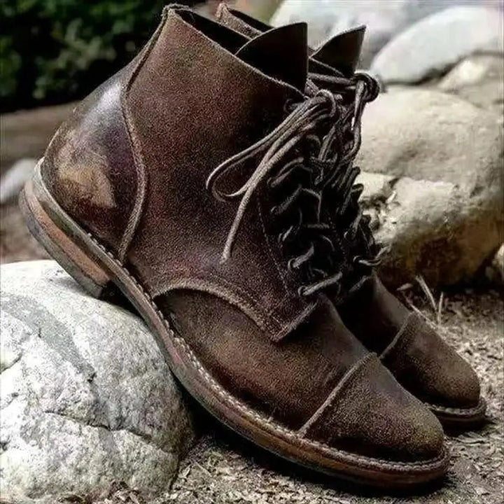 Chocolate cap toe boots with a worn-in finish resting on rocks