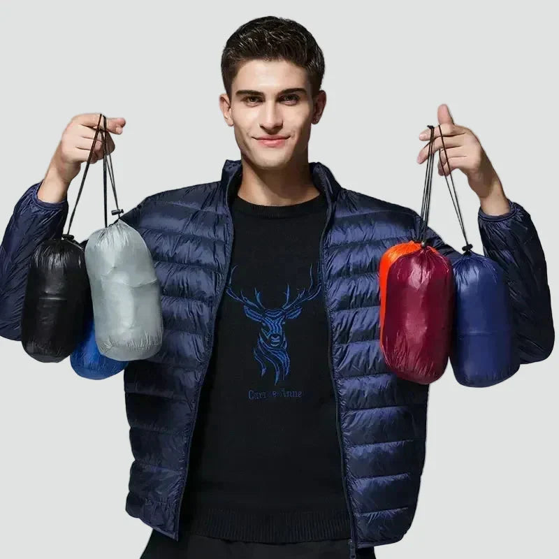 Man wearing the navy puffer jacket and holding the jackets packed into small pouches