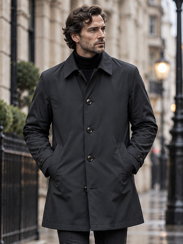 Black mid length mac coat worn with a black roll neck on a lamp-lit street