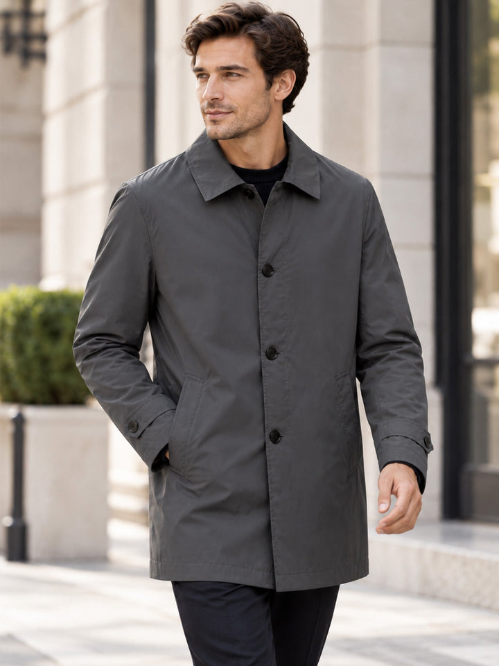 Man in a grey mid length coat with hands in pockets on a city street