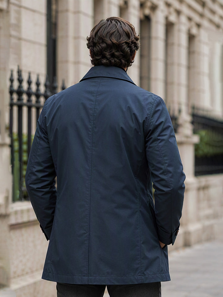 Back view of a navy single breasted mac coat on a city street