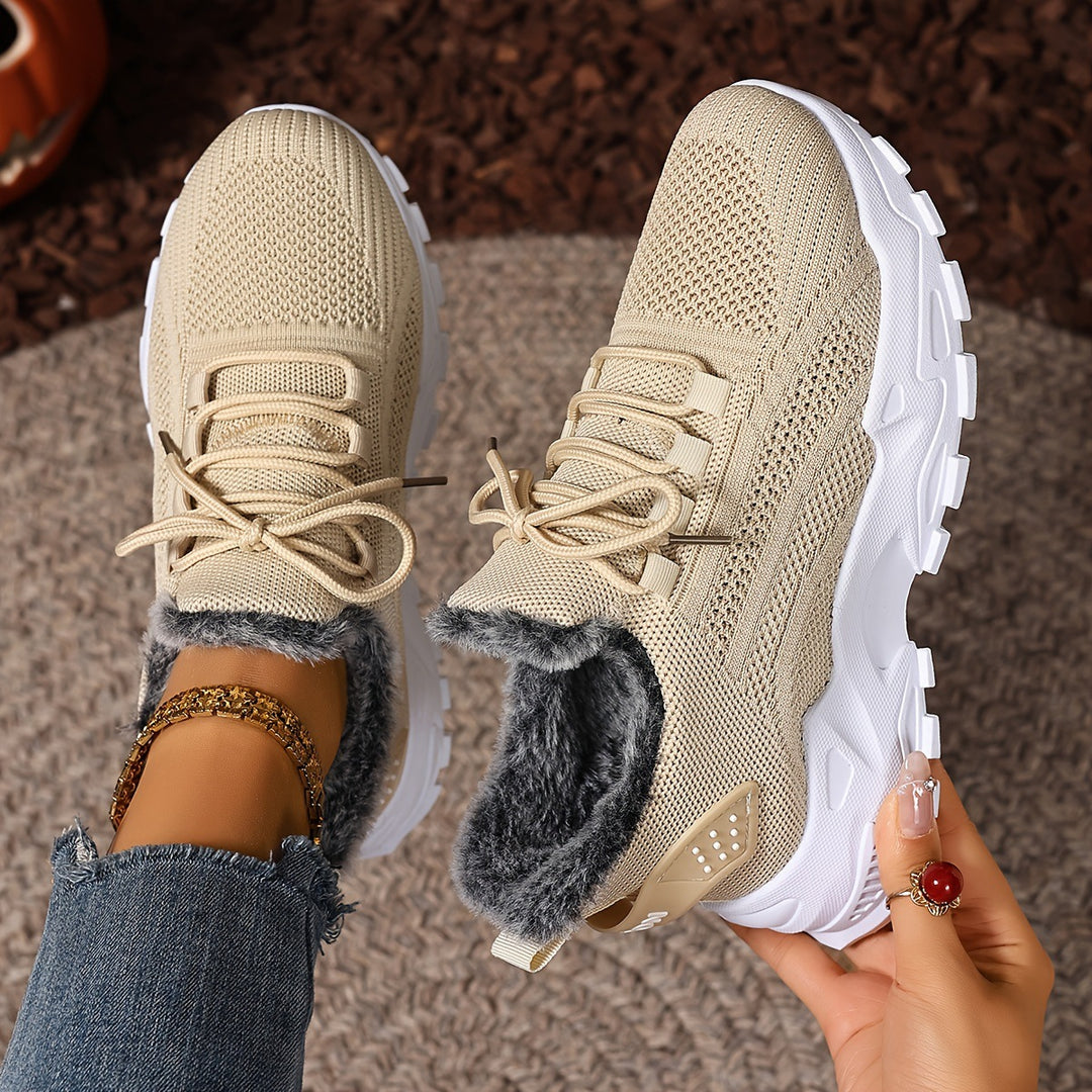 Beige trainers, held up to show the inside and the sole