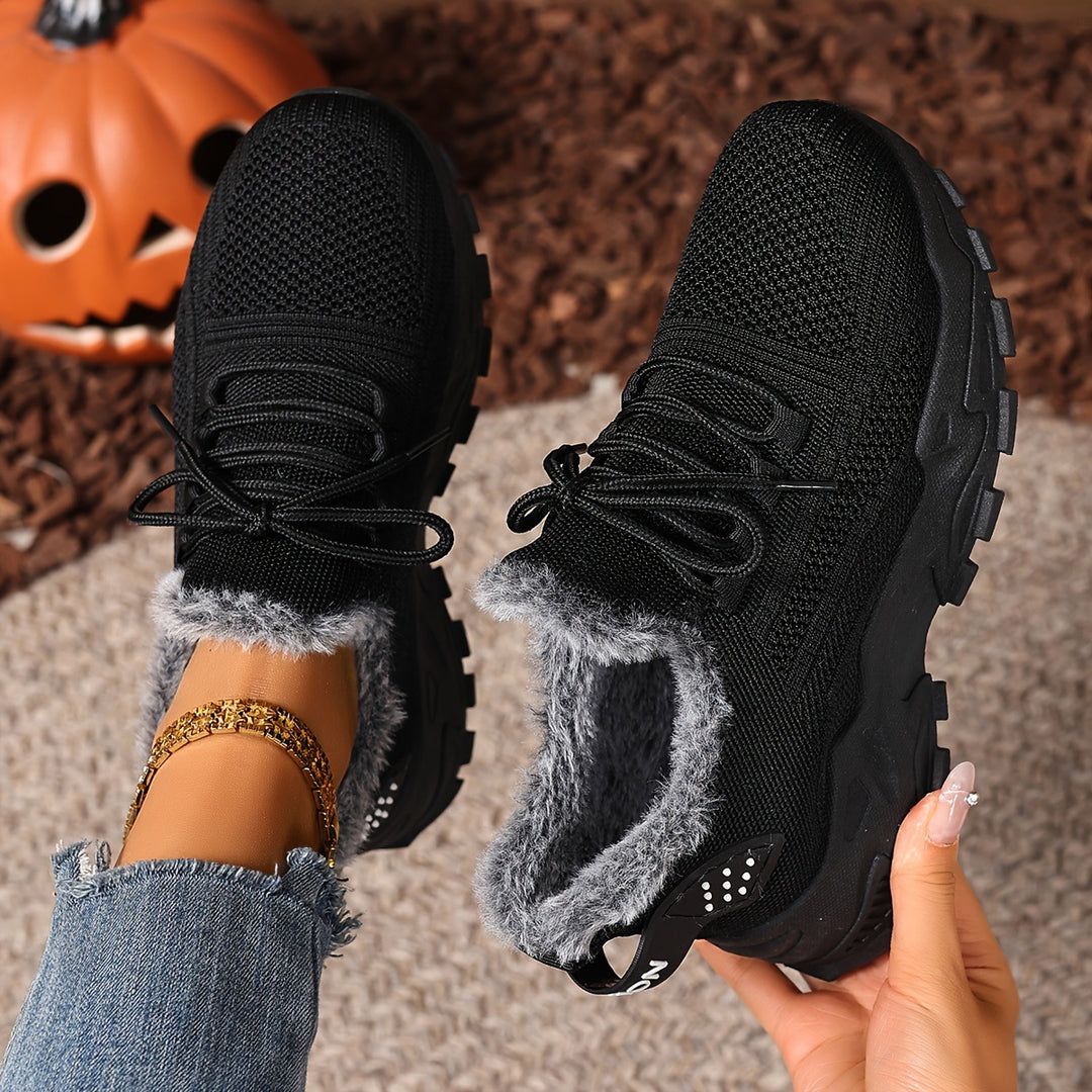 Black trainers, held up to show the inside and the sole