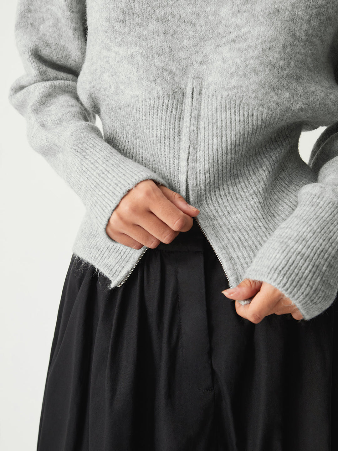 Close view of the zip at the front hem of the grey jumper