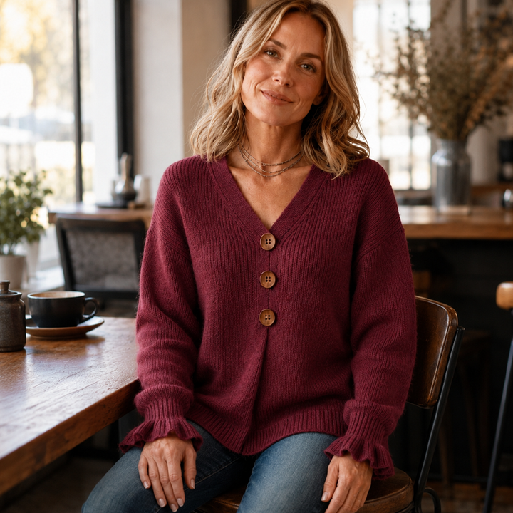 Burgundy button front jumper with V neck worn seated at a wooden table