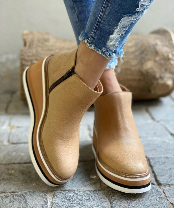 Beige ankle boots with a layered striped wedge sole on cobbles
