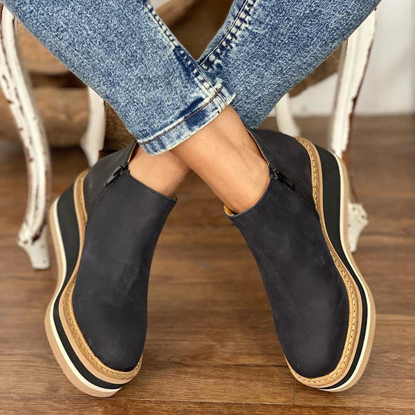 Dark wedge boots worn with crossed legs on a wooden floor