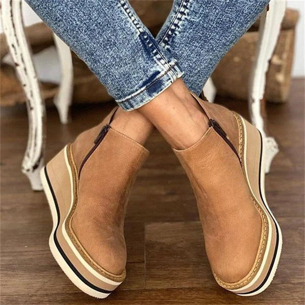 Tan wedge boots worn with crossed legs and cuffed trousers