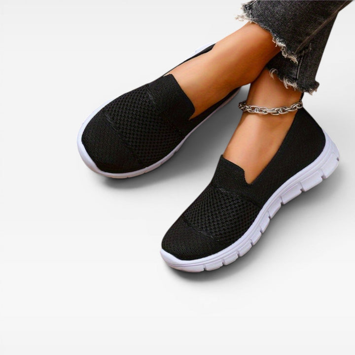 Model crossing her feet in black knit slip on trainers